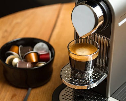 Copenhagen, Denmark - July 8, 2014: Freshly brewed espresso in glass standing on silver Nespresso coffe machine. Blurred background with Nespresso capsules in black bowl.